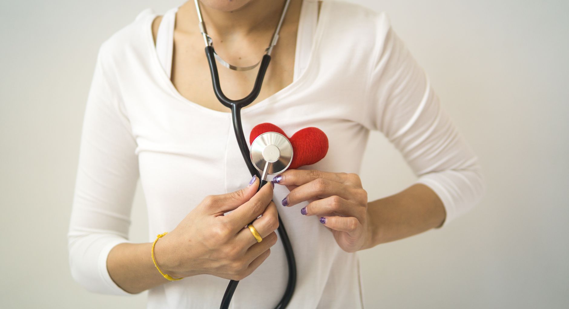 Unrecognizable female wearing white shirt while standing on white background with diaphragm of stethoscope on red handmade he