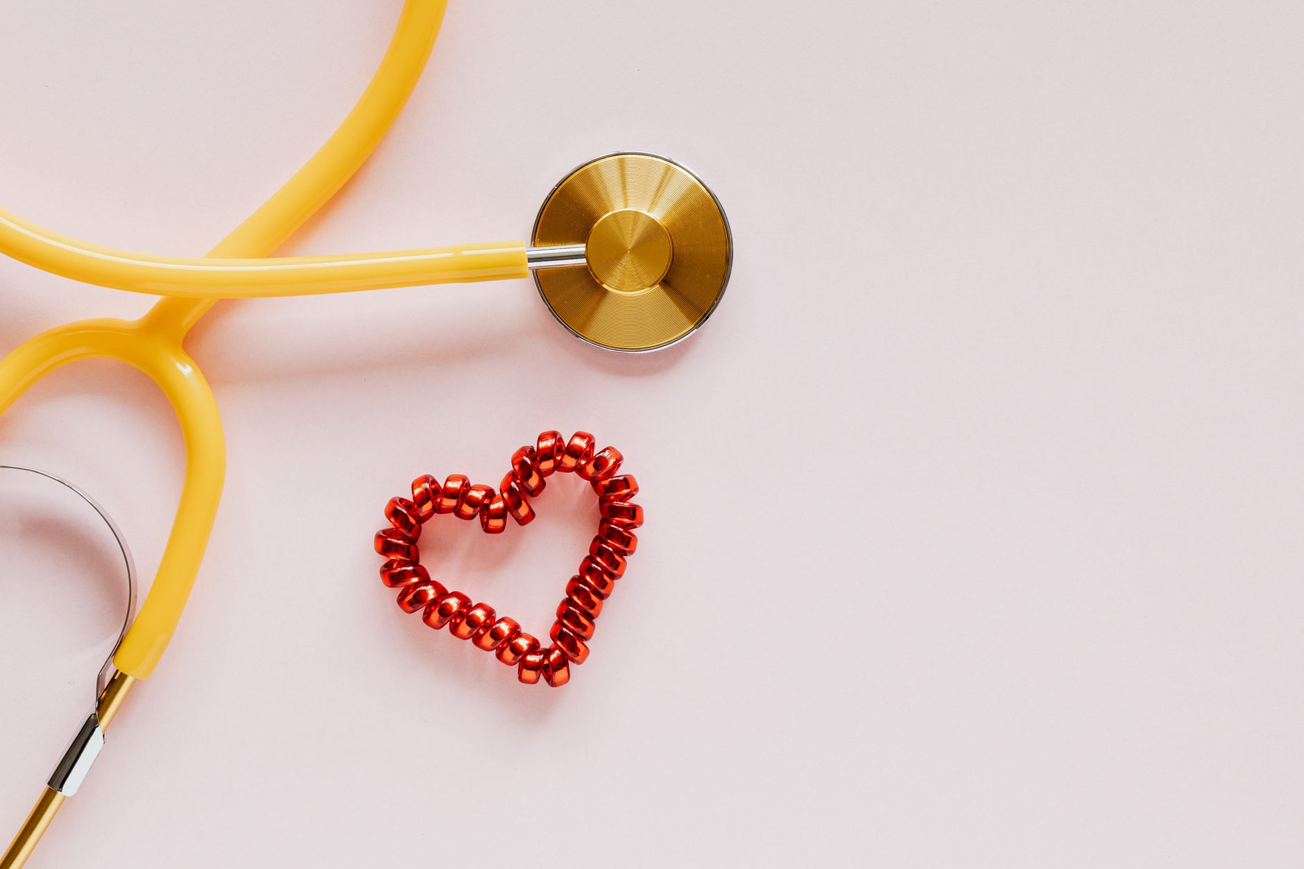 From above of yellow stethoscope near small red bead heart made for San Valentines Day on pale pink surface — A Simple Guide