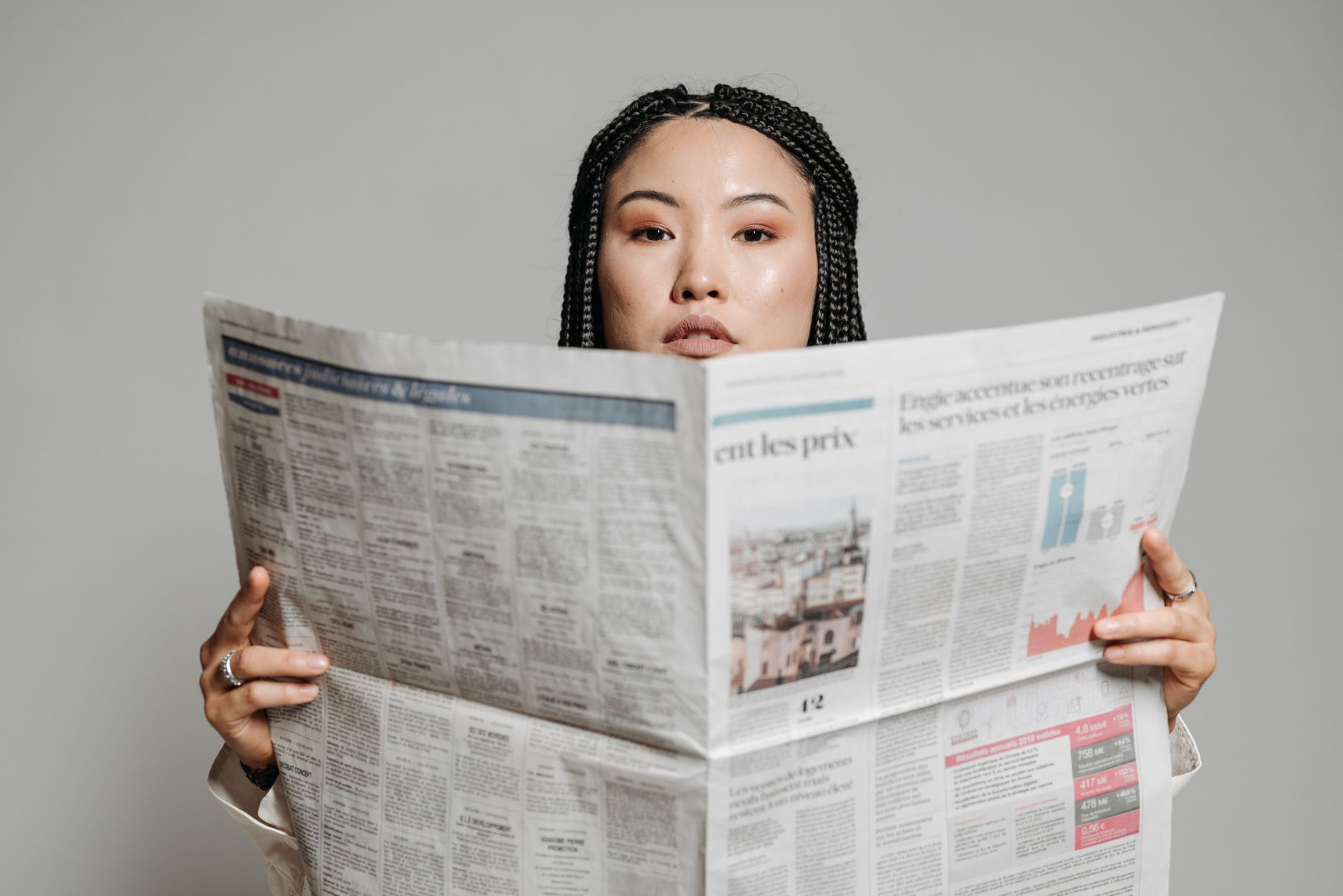 Asian woman with braided hair reading a newspaper in a studio setting. — Achieving a Natural-Looking Smile with Dental Implan