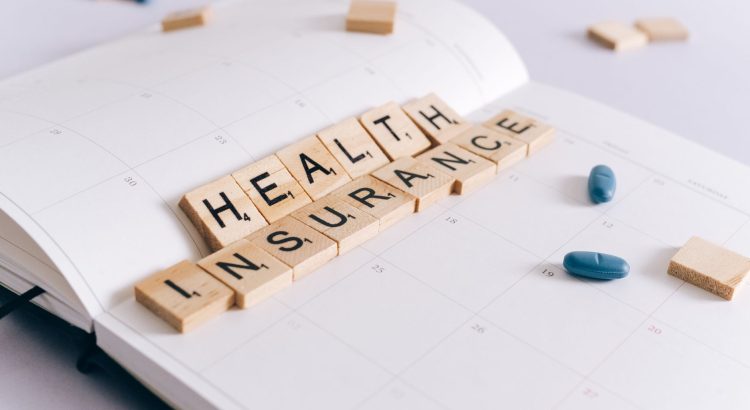 Scrabble tiles spelling 'Health Insurance' on a calendar with pills. — Athem Blue Mix Offering Two New Medical Health Insuran