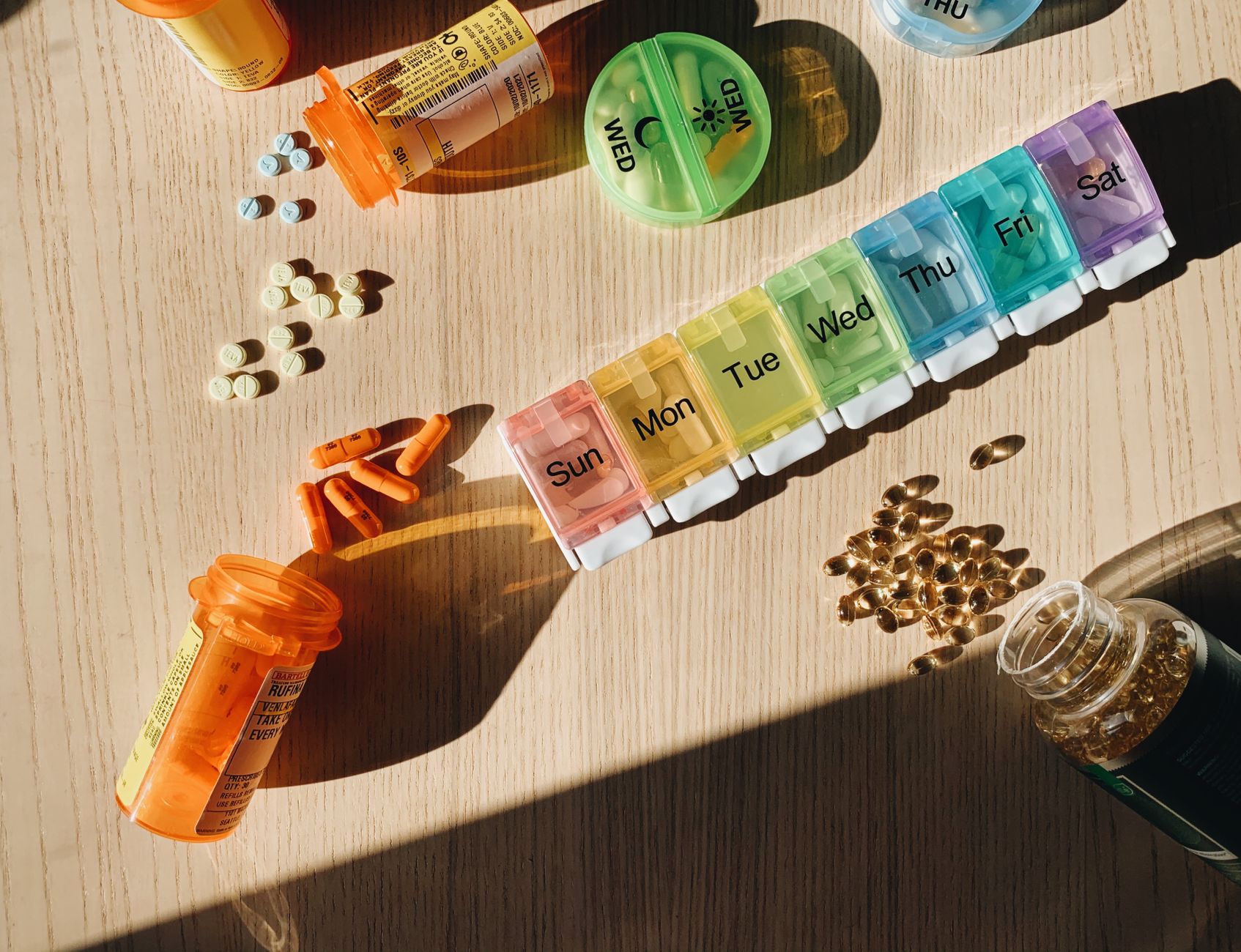 Colorful pill organizer with medication bottles and tablets on a wooden surface. — Building Green house - Evaluating the tric