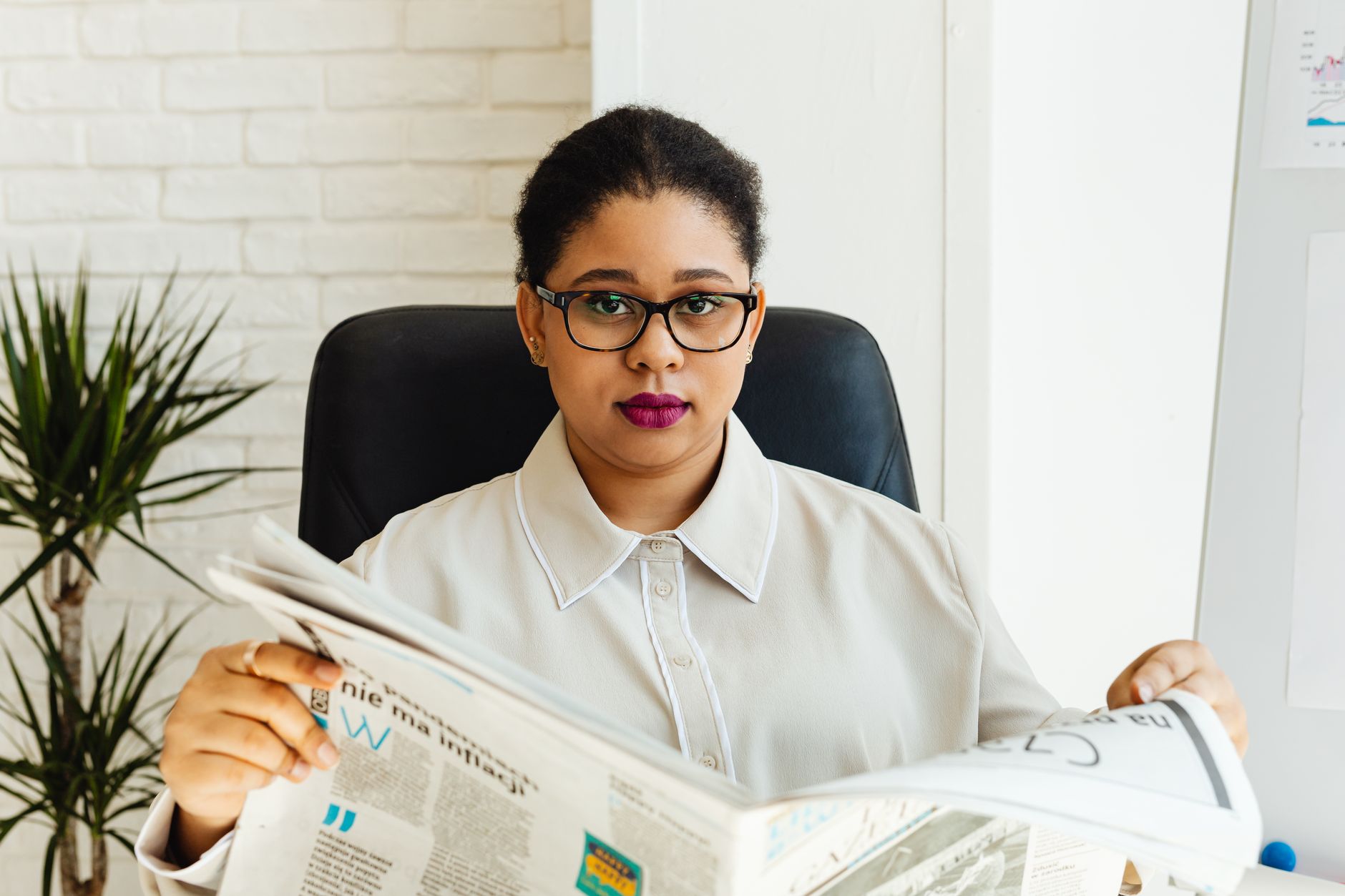 Professional woman with glasses reading a newspaper at her office desk, surrounded by modern decor. — Casino akcije online