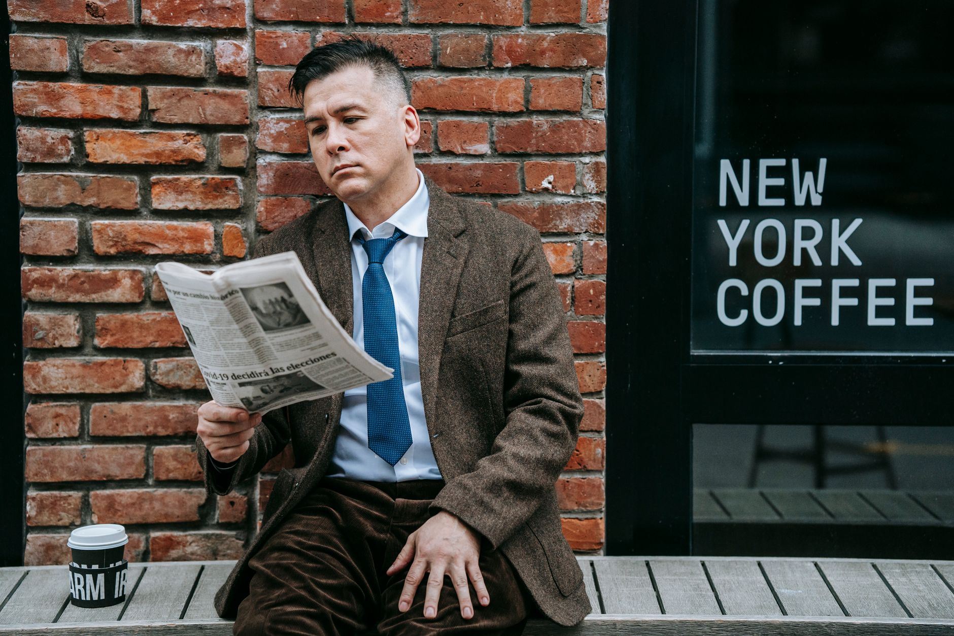 A professional man in formal wear reads a newspaper beside a coffee shop window. — DAMAGES CAUSED BY STRIKING SPEED BUMPS AT