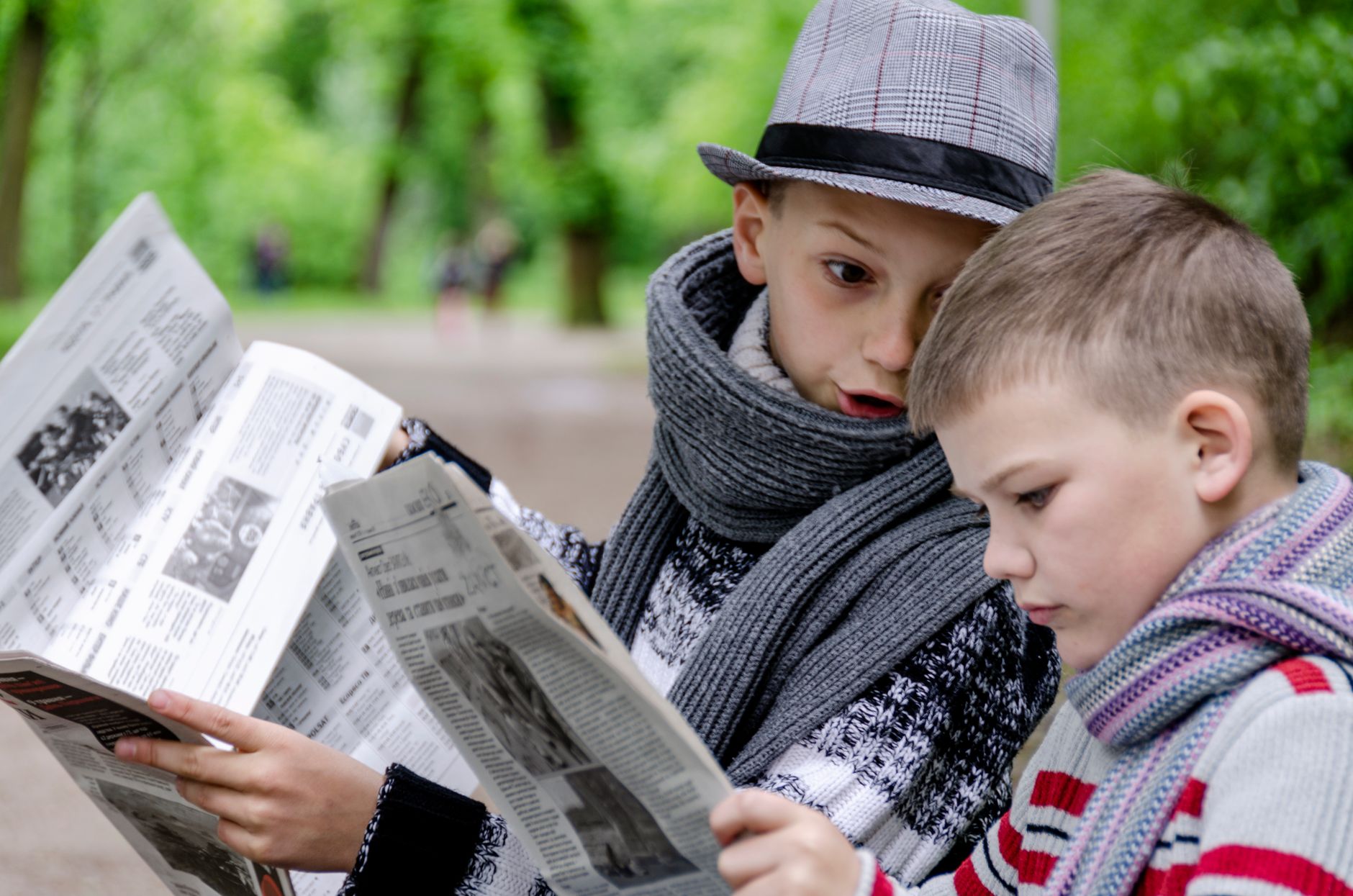 Two young boys reading newspapers together in a lush green park in Lviv, Ukraine. — Dr Michael Hilton: Essential Qualities of