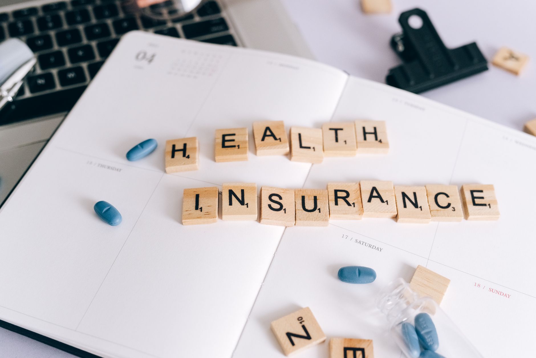Scrabble tiles spelling 'Health Insurance' on planner with pills and laptop, symbolizing healthcare planning. — Exercises to