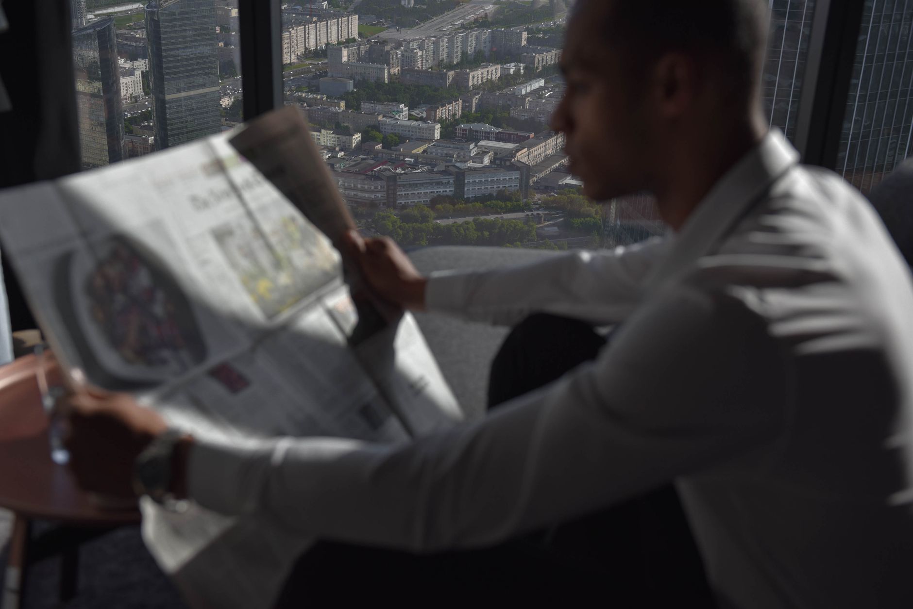 A man in a white shirt reads a newspaper with a high-rise city view. — Exploring that tips to follow for the purchase of fake