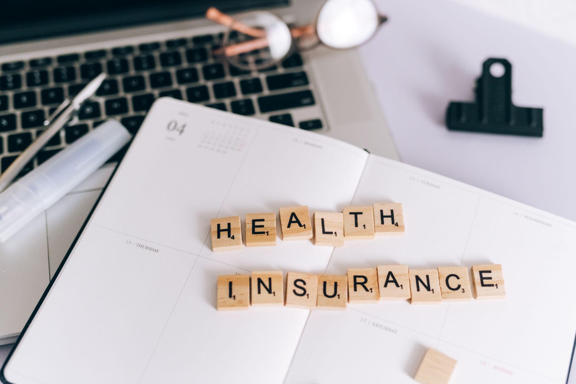 Close-up of Scrabble tiles spelling 'Health Insurance' on a planner with a laptop. — Hair Care Routine for the Ultimate Style