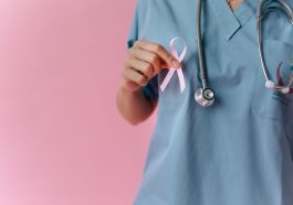 Healthcare worker in scrubs holds a pink breast cancer awareness ribbon symbolizing support. — Health Reform Through Preventi