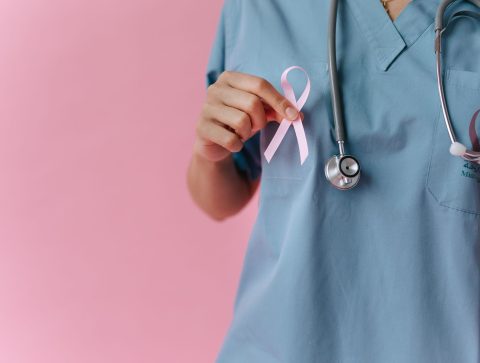 Healthcare worker in scrubs holds a pink breast cancer awareness ribbon symbolizing support. — Health Reform Through Preventi