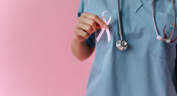 Healthcare worker in scrubs holds a pink breast cancer awareness ribbon symbolizing support. — Health Reform Through Preventi