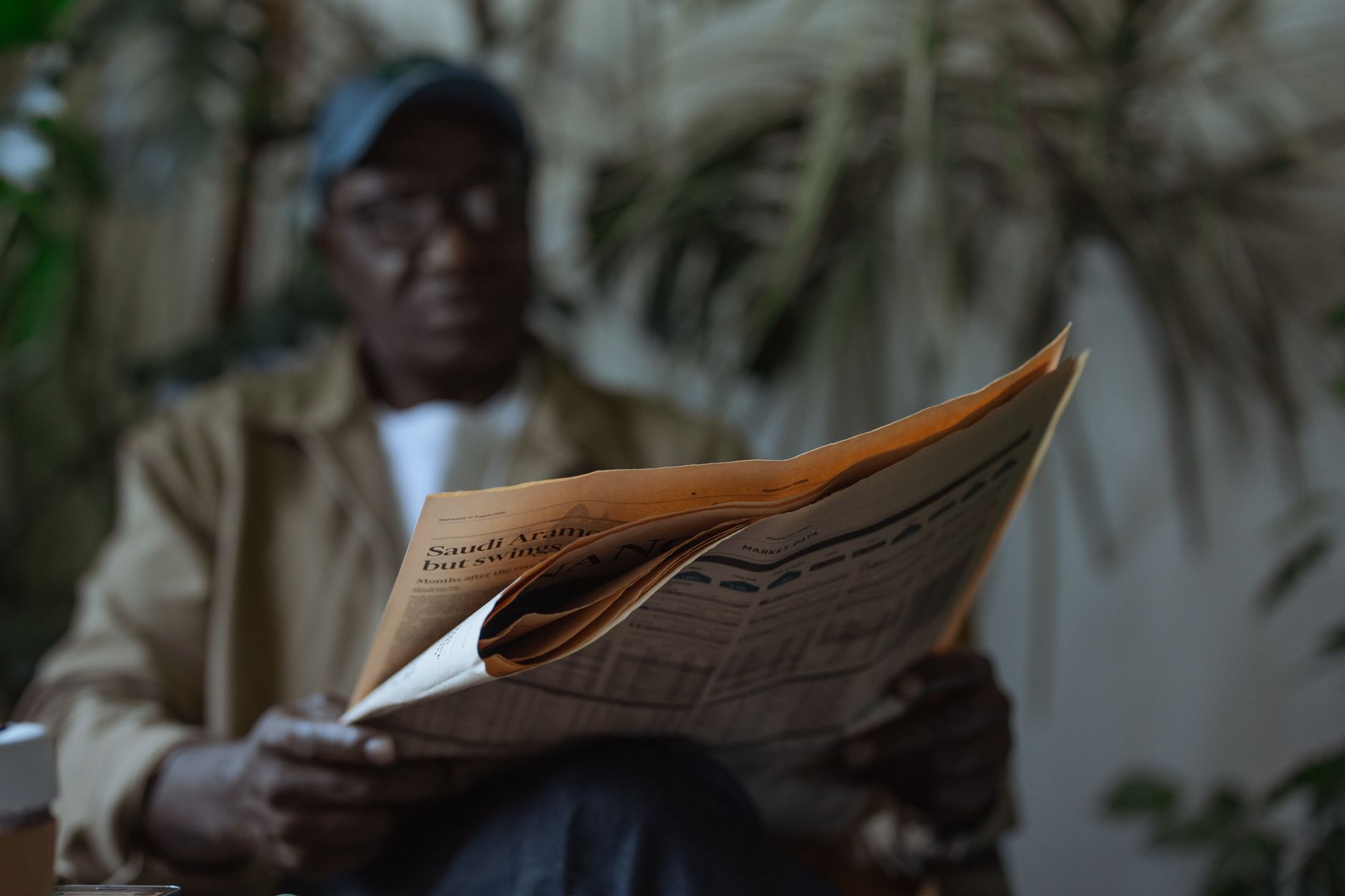 An adult man reading a newspaper indoors, surrounded by plants with a blurred background. — How Shared Interests Predict Comp