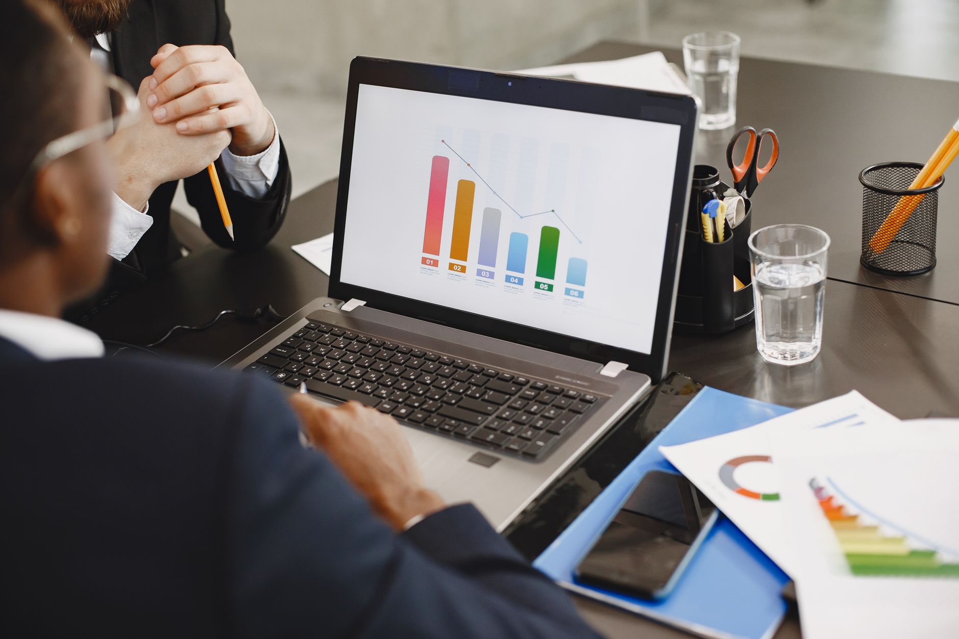 Two professionals analyzing a business graph on a laptop during a meeting. — Influence Marketing Agencies: Fostering Authenti