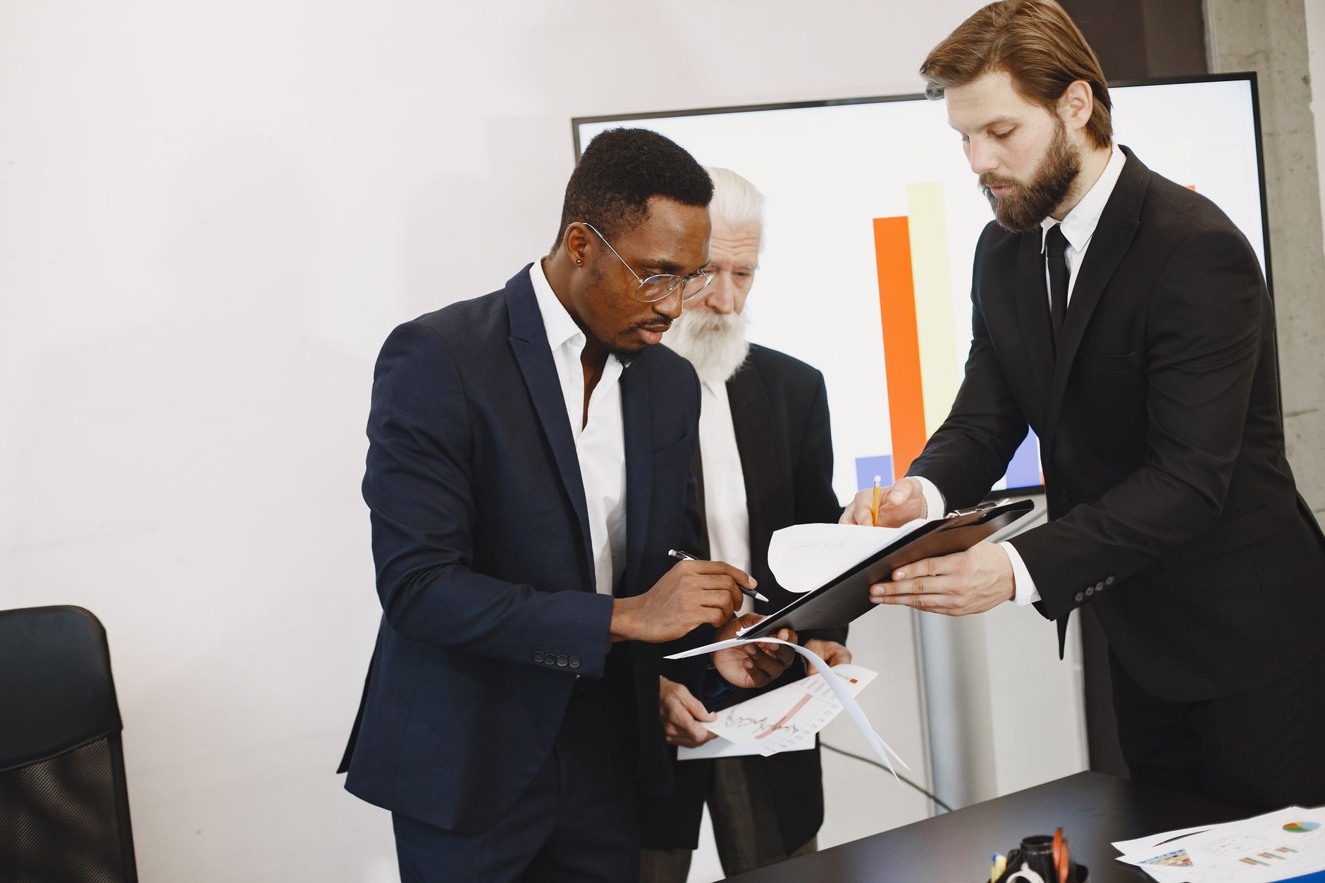 Three businessmen engaged in document signing in a modern office setting. — Insider's Experience: What it's Like to Teach Eng
