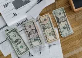 Stacks of US Dollar banknotes placed over financial documents and reports on a desk. — IronFX User Experience: A Practical Gu