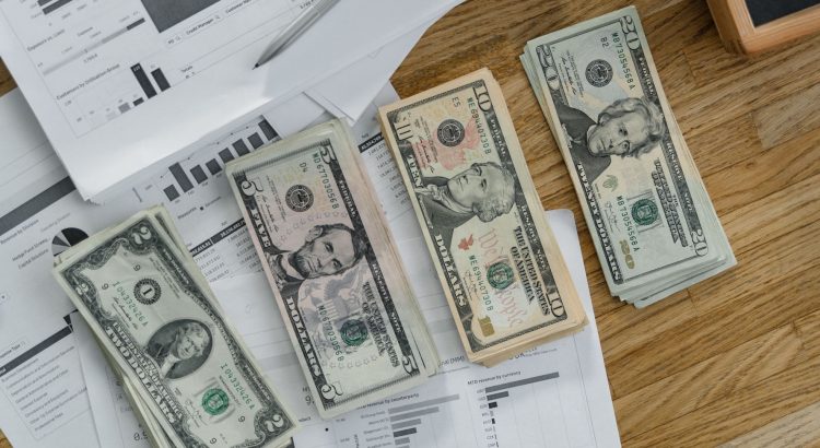Stacks of US Dollar banknotes placed over financial documents and reports on a desk. — IronFX User Experience: A Practical Gu