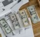 Stacks of US Dollar banknotes placed over financial documents and reports on a desk. — IronFX User Experience: A Practical Gu