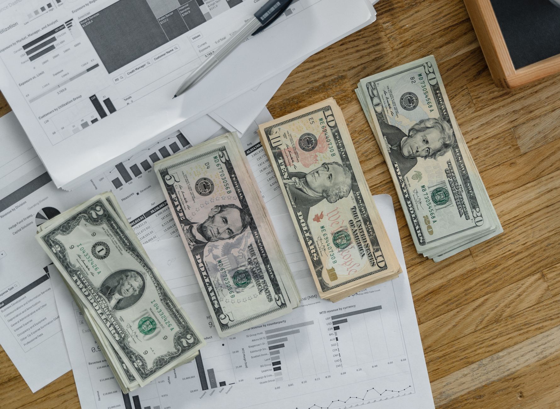Stacks of US Dollar banknotes placed over financial documents and reports on a desk. — IronFX User Experience: A Practical Gu