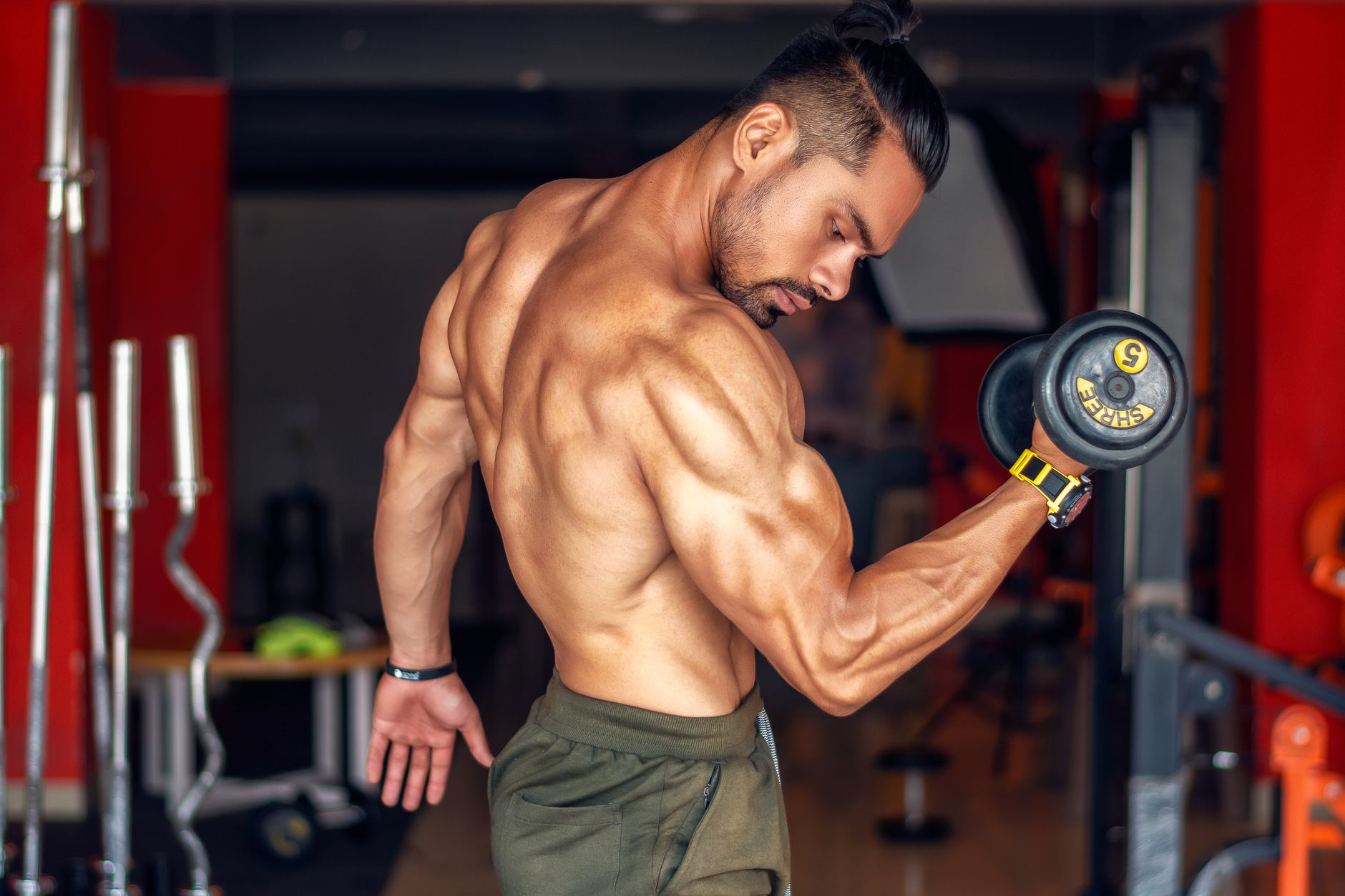 A fit, shirtless man showcasing biceps while lifting a dumbbell in a gym setting. — Livestrong Fitness Review