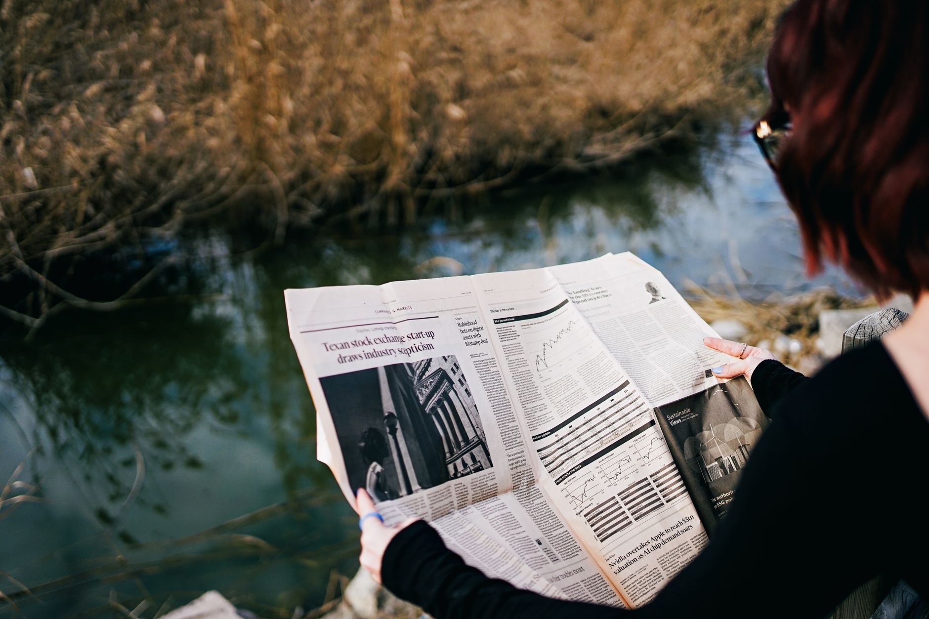 A woman reads a newspaper by a river surrounded by autumn foliage. — Medicare Advantage in 2024: Significant Developments You