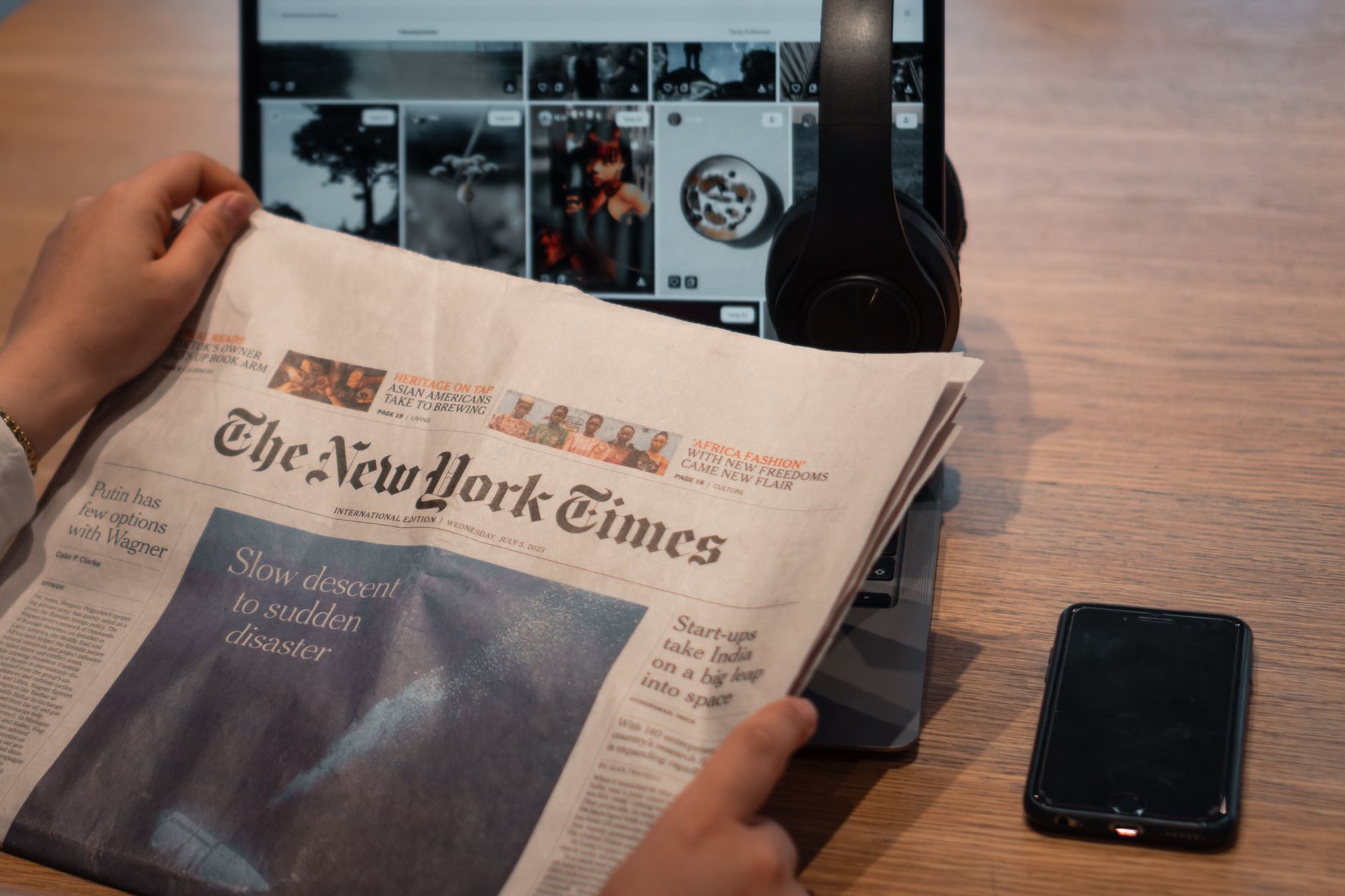 Close-up of hands holding a newspaper by a laptop and smartphone on a table. — Medicare Advantage Plans:How They Can Benefit
