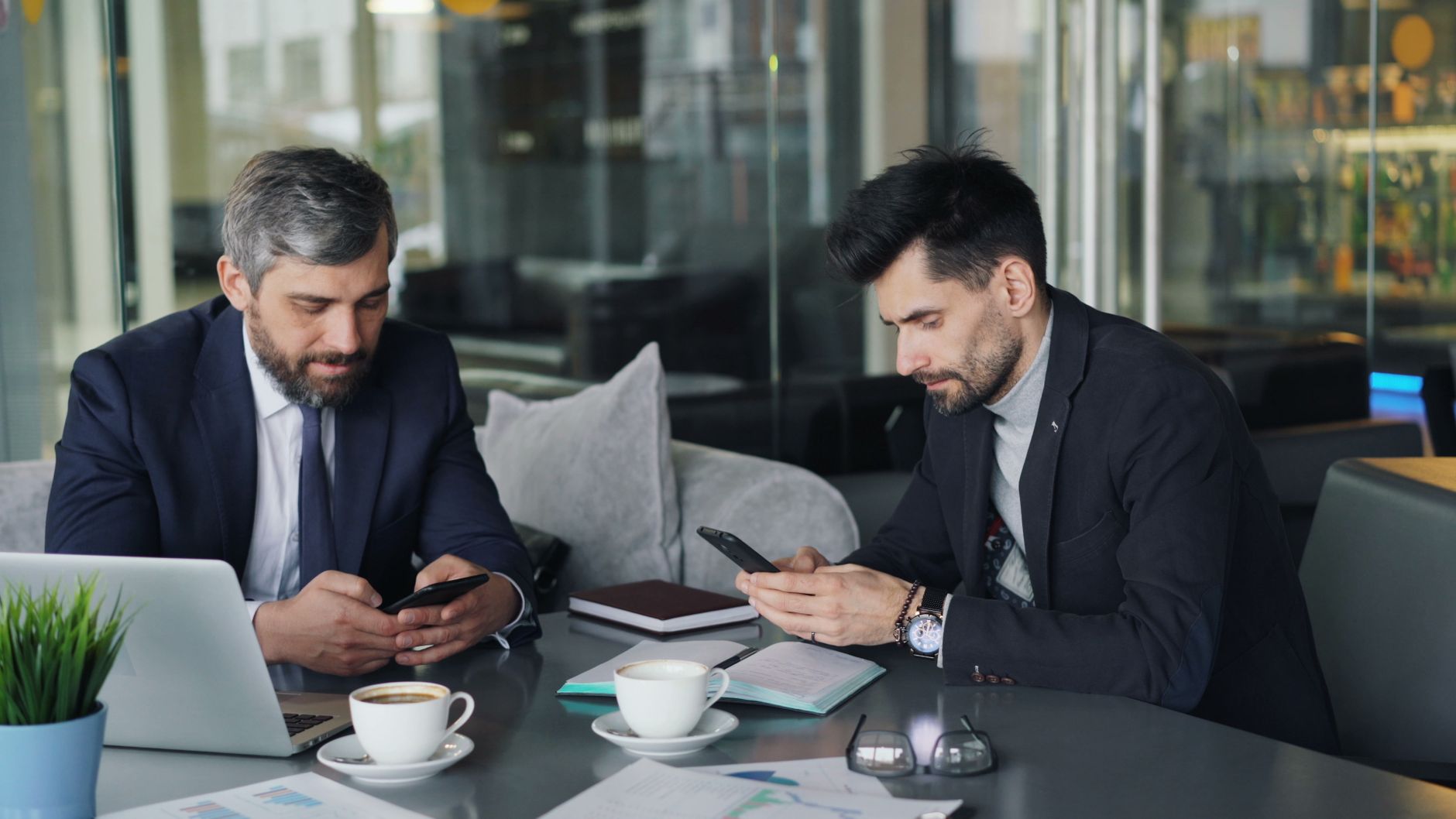 Two businessmen in a cafe working on smartphones and laptops, engaged in a meeting. — Melaleuca Health and Wellness: A Path t