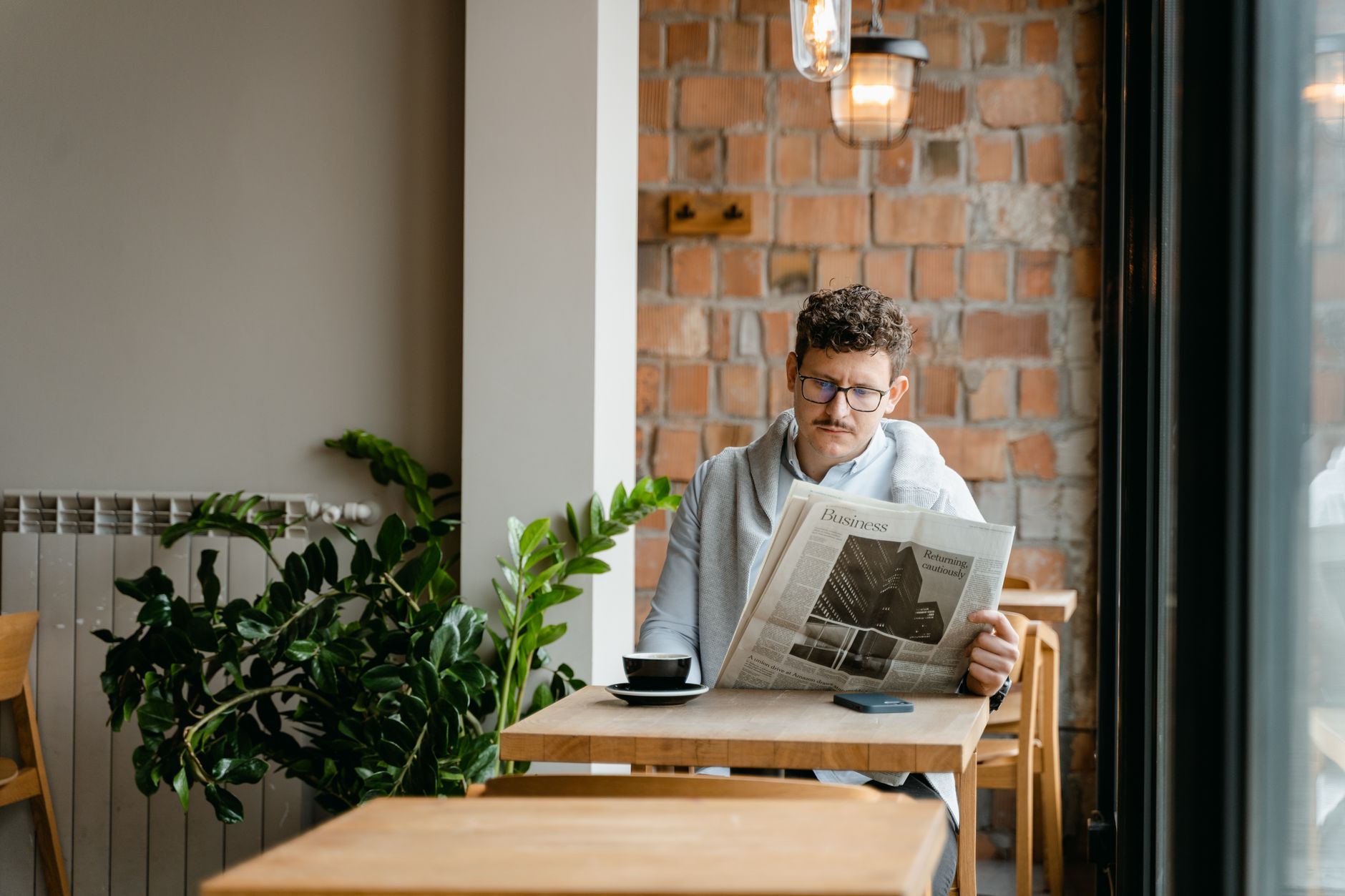 A man with glasses enjoys coffee and reads a newspaper in a cozy café setting. — The Ultimate Guide to weed delivery Vancouve