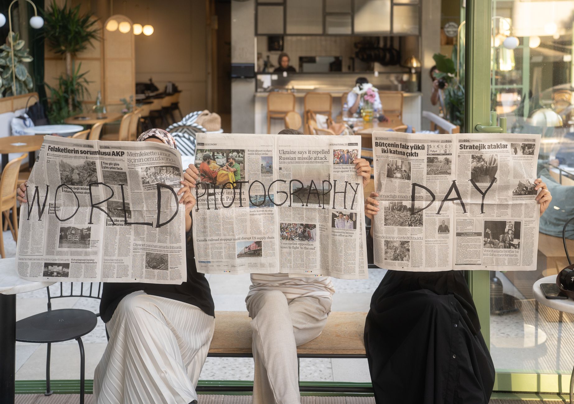 Three people holding newspapers promoting World Photography Day in a cozy Ankara café. — The wall mounted wire shoe rack: Hel