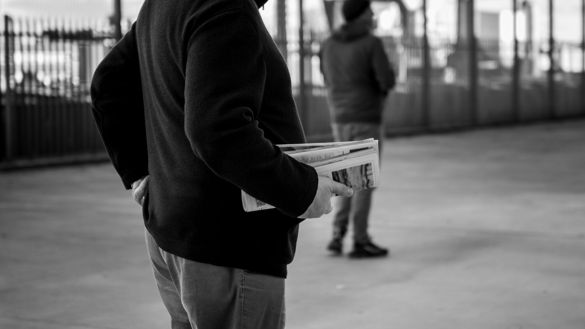 A monochrome image of a person holding newspapers in an urban environment, capturing the essence of street life. — Top Reason