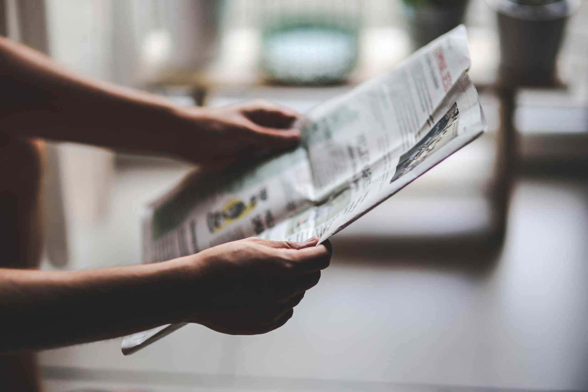Hands holding a newspaper in a soft-lit, indoor environment, focusing on a relaxed reading moment. — Tune Into Opportunities: