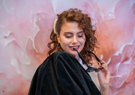 Stylish woman with curly hair poses with sunglasses against a pink floral backdrop. — Updating Your Salon For Today's Cliente