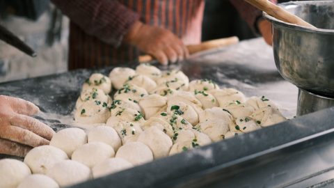 Close-up of hands shaping fresh dough balls with herbs at a bakery counter. — What's Within The Food You're Eating, And Which