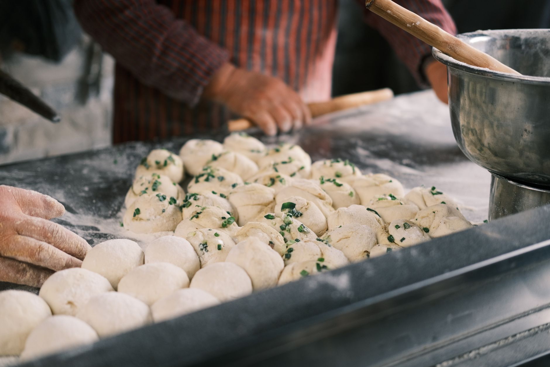 Close-up of hands shaping fresh dough balls with herbs at a bakery counter. — What's Within The Food You're Eating, And Which