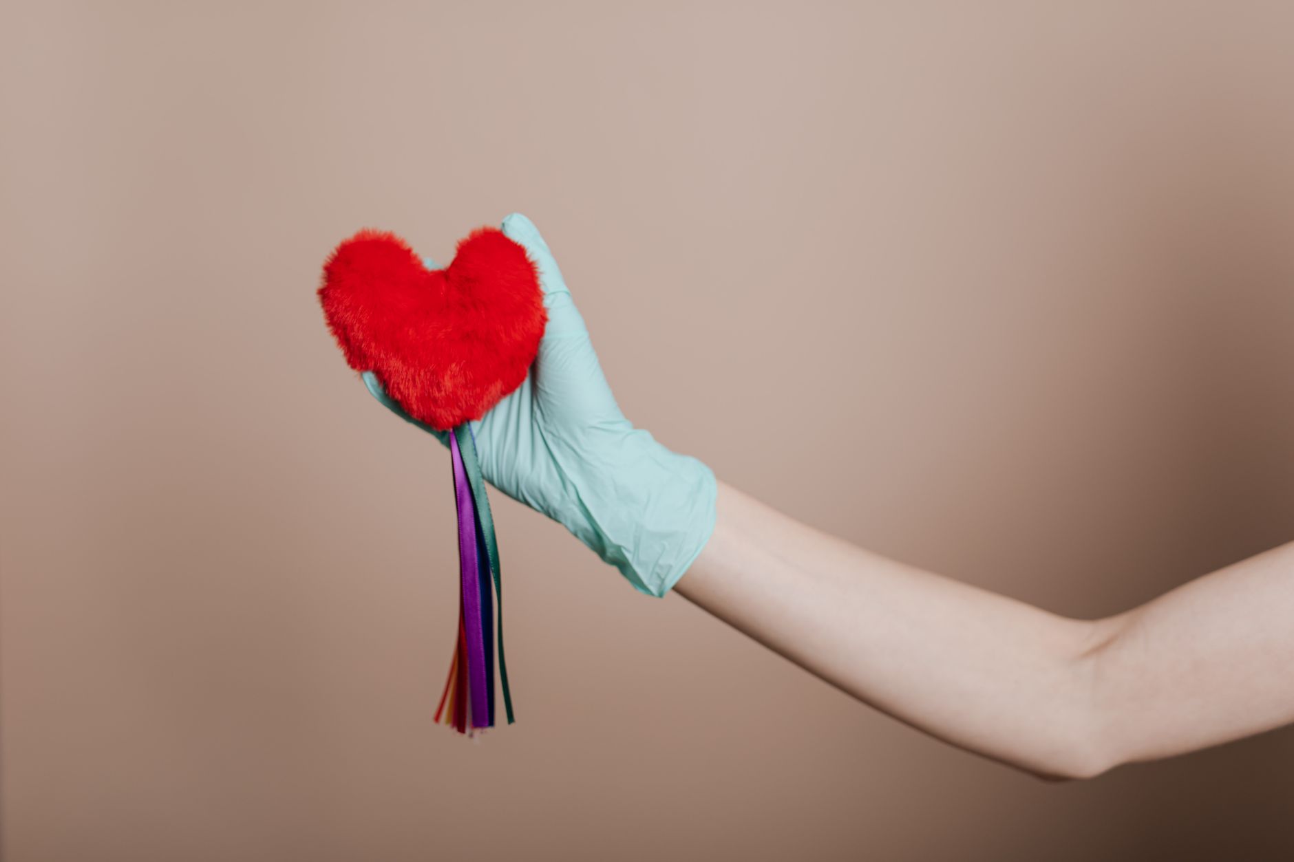 A latex-gloved hand holds a red heart-shaped plush with colorful strings, symbolizing love and safety. — What You Need To Kno