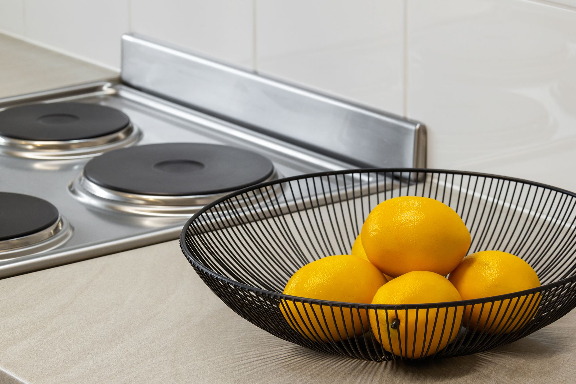 Lemons in a metal bowl on a kitchen counter beside an electric stove, highlighting freshness and simplicity. — Where to shop
