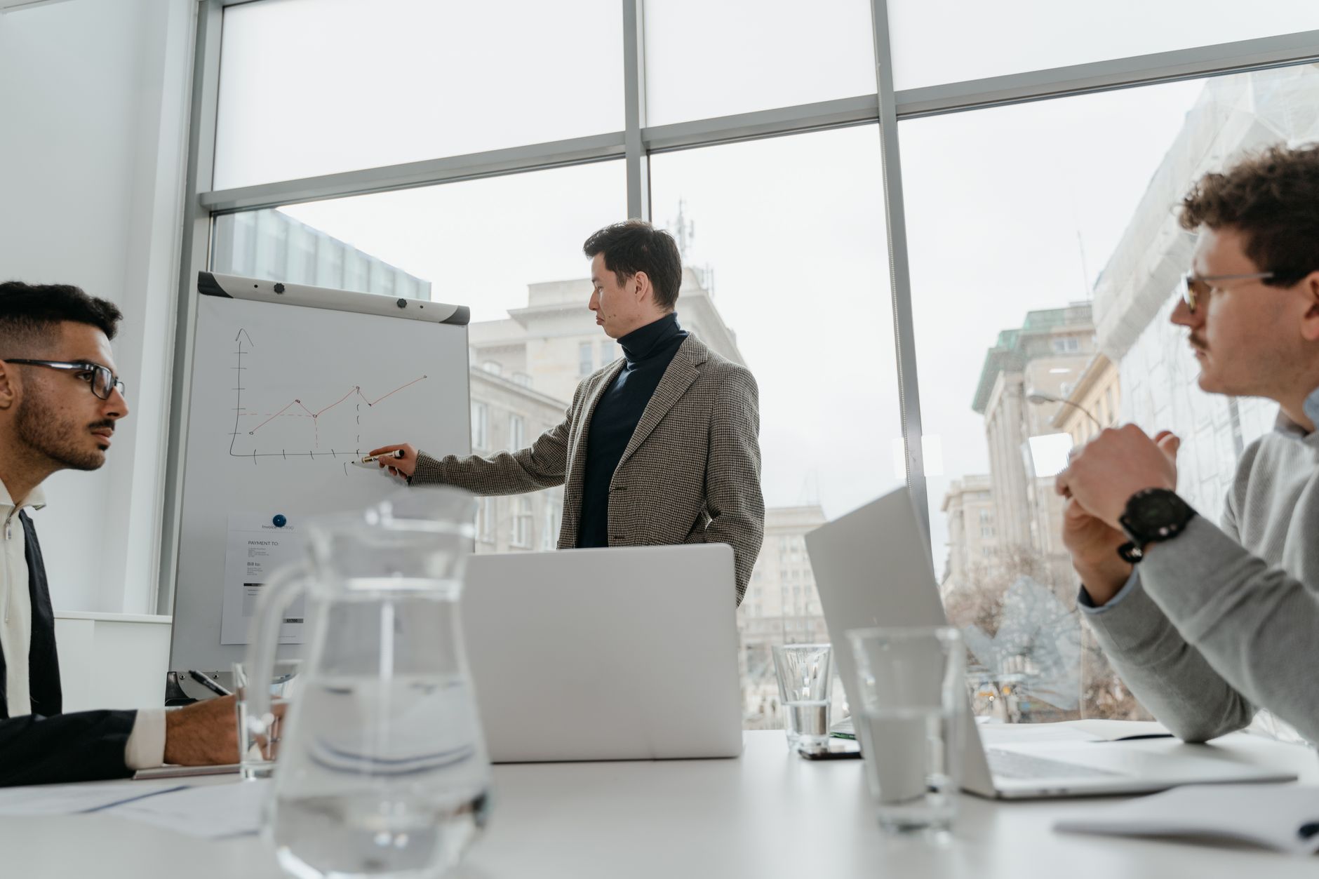 Professionals engaged in a collaborative business meeting with charts and laptops in a modern office setting. — Why Certifica